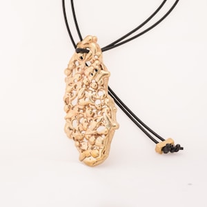 May include: A gold pendant necklace with a delicate, intricate design. The pendant is made of a textured metal and hangs from a black cord.