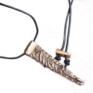 May include: A silver pendant necklace with a textured, leaf-shaped design hangs from a black leather cord. The cord has a small, gold-colored clasp.