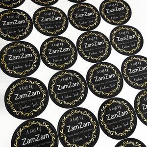 May include: A sheet of black and gold round stickers with the text "A Gift of ZamZam" and "Please Keep Us In Your Duas" in a gold ornate font.