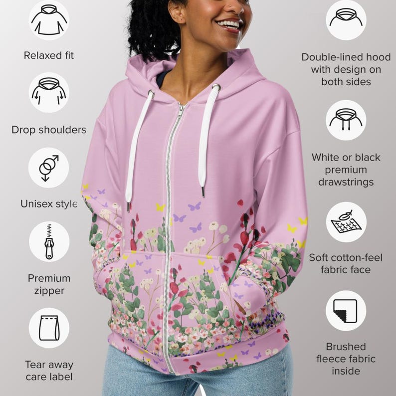 May include: A light pink unisex zip-up hoodie with a floral design featuring red, white, and green flowers, and yellow and purple butterflies. The hoodie has a relaxed fit, drop shoulders, a premium zipper, and white drawstrings. It has a soft cotton-feel fabric face and a brushed fleece fabric inside.