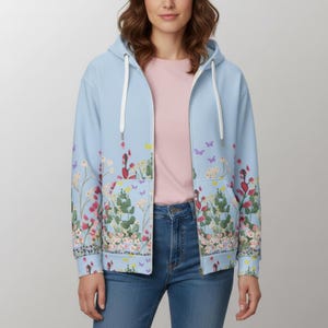 May include: A light blue zip-up hoodie with a floral and butterfly design. The hoodie features a white drawstring and pockets. The floral pattern includes red, pink, and green flowers with purple and yellow butterflies.