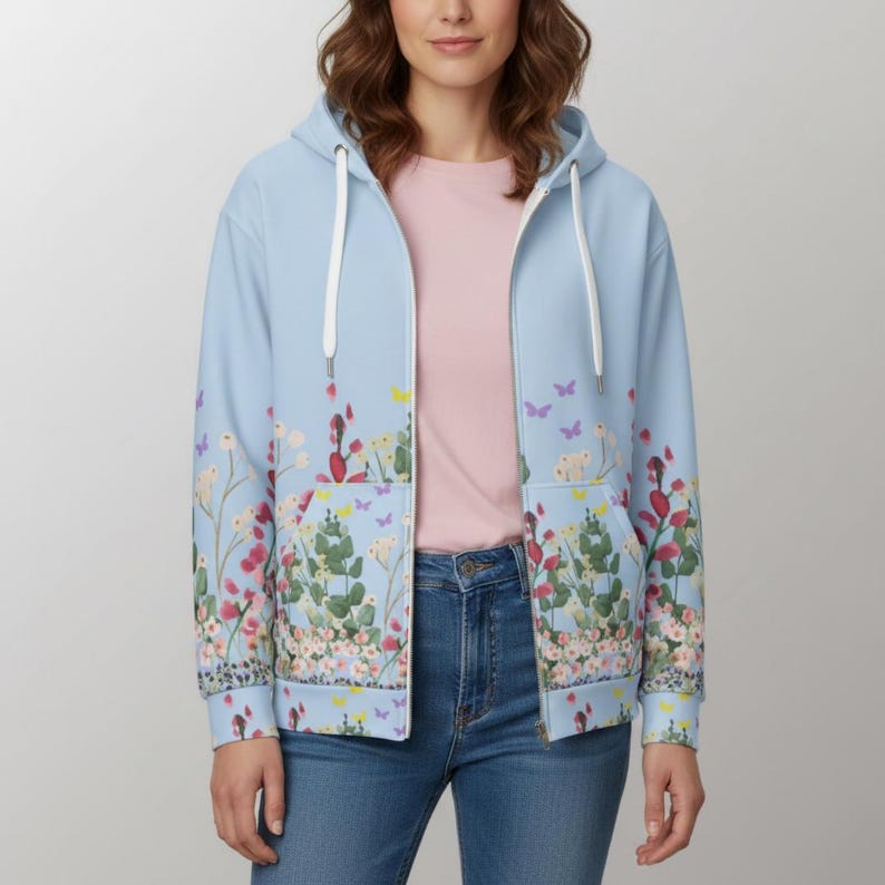 May include: A light blue zip-up hoodie with a floral and butterfly design. The hoodie features a white drawstring and pockets. The floral pattern includes red, pink, and green flowers with purple and yellow butterflies.