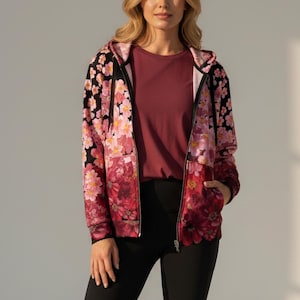May include: A zip-up hoodie with a floral pattern in shades of pink and red, set against a black background. The hoodie is paired with a burgundy t-shirt and black leggings. The jacket has a hood and pockets.