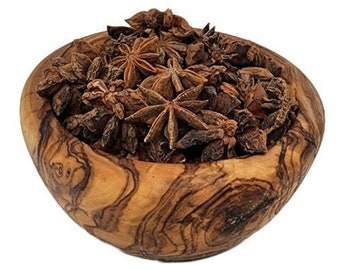 Op de afbeelding: Een houten kom gevuld met steranijs. De kom is gemaakt van olijfhout en vertoont een natuurlijk houtnerfpatroon. De steranijs heeft een diepbruine kleur, met een stervorm. De afbeelding is tegen een witte achtergrond.