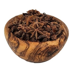 May include: A wooden bowl filled with star anise. The bowl is made of olive wood, displaying a natural wood grain pattern. The star anise is a deep brown color, with a star-like shape. The image is set against a white background.