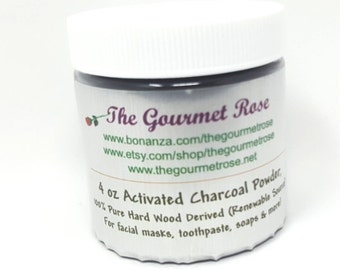 Op de afbeelding: Een cilindervormige pot met een witte deksel, met het label "The Gourmet Rose". Het etiket bevat websiteadressen en de tekst: "4 oz Activated Charcoal Powder, 100% Pure Hard Wood Derived". De pot is gevuld met zwart poeder.
