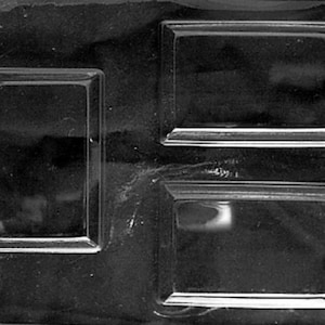 May include: A black plastic mold with three rectangular cavities. The mold is designed for creating shaped items, possibly for crafts or food decoration. The cavities have raised edges.