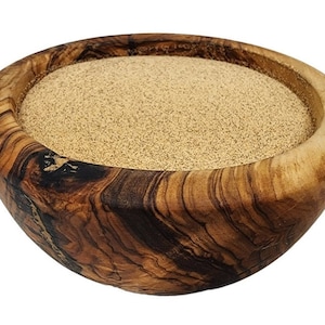 May include: A wooden bowl filled with a light brown, granular substance. The bowl is made of olive wood, showcasing a rich, natural grain pattern with dark brown and tan hues. The bowl's interior is filled with a fine, powdery material.