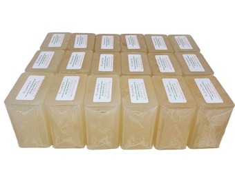 Puede incluir: Una colección de barras de jabón rectangulares de color amarillo claro, cada una envuelta en plástico transparente. Cada barra tiene una etiqueta blanca con texto. Las barras están dispuestas en filas ordenadas.