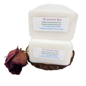 Puede incluir: Dos barras de jabón de manteca de karité cuadradas apiladas, de color blanquecino, con etiquetas de "The Gourmet Rose". Una rosa roja oscura seca descansa junto a los jabones. Las etiquetas dicen "1 lb SHEA BUTTER All Natural Melt & Pour Soap."
