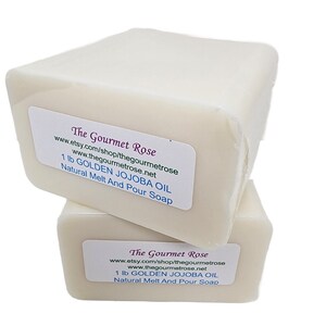 Op de afbeelding: Twee ivoorkleurige rechthoekige zeepblokken op elkaar gestapeld. Elk blok heeft een label met de tekst "The Gourmet Rose", websiteadressen en "1 lb GOLDEN JOJOBA OIL Natural Melt And Pour Soap".