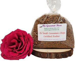 Könnte beinhalten: Ein klarer Plastikbeutel gefüllt mit kleinen Zimtstückchen, beschriftet mit "1 lb Small Cinnamon Chips Certified Kosher". Links vom Beutel befindet sich eine leuchtend rote Rose. Der Beutel steht auf einer Holzscheibe.