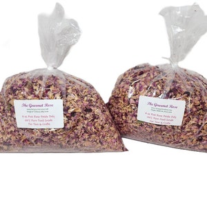 May include: Two clear plastic bags filled with dried pink rose petals. Each bag has a white label with the text "The Gourmet Rose" and product information. The bags are sealed at the top, showcasing the petals.