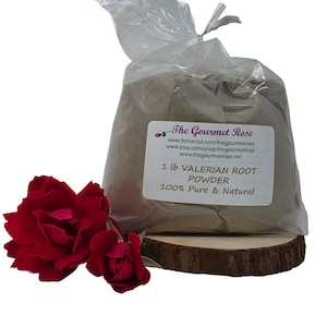 Puede incluir: Una bolsa de plástico transparente llena de polvo de raíz de valeriana, etiquetada como 1 lb, descansa sobre una rodaja de madera. La etiqueta también indica que el polvo es 100% puro y natural. Dos rosas rojas están a la izquierda.