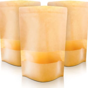 May include: Three stand-up pouches with a kraft paper appearance. Each pouch has a clear, horizontal window near the bottom. The pouches are empty and ready for filling. The background is white.