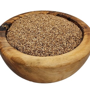May include: A wooden bowl filled with small, light brown seeds. The bowl is made of light-colored wood with a visible grain. The seeds fill the bowl to the top, creating a textured surface. The background is plain white.