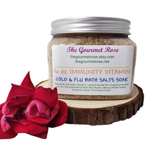 May include: A clear glass jar with a silver lid, filled with bath salts. The label reads "The Gourmet Rose" and "16 oz Immunity Vitamin Cold & Flu Bath Salts Soak." A red rose and a wooden slice are in the foreground.