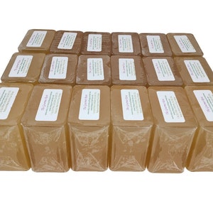 May include: A collection of rectangular, light brown soaps, individually wrapped in clear plastic. Each soap has a white label with text. The soaps are arranged in neat rows, creating a visually appealing display.