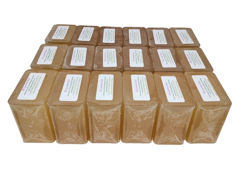 May include: A collection of rectangular, light brown soaps, individually wrapped in clear plastic. Each soap has a white label with text. The soaps are arranged in neat rows, creating a visually appealing display.