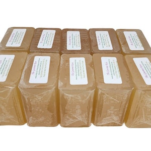 May include: A collection of rectangular, light amber-colored soaps, individually wrapped in clear plastic. Each soap has a white label with text. The soaps are arranged in a neat, stacked formation, showcasing a natural, handcrafted aesthetic.