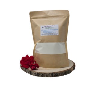 May include: A brown paper bag with a white window, containing a powder, sits on a wooden slice. A red rose is placed in front of the bag. The bag has a label that reads "The Gourmet Rose" and lists the product as "Organic Hydrolyzed Marine Collagen Peptides, Type I."