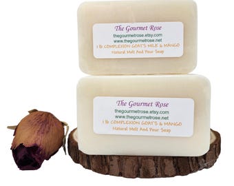 Könnte beinhalten: Zwei rechteckige Blöcke Naturseife, beschriftet mit "The Gourmet Rose", sind auf einem Holzsockel gestapelt. Jeder Block hat ein weißes Etikett mit Text. Links ist eine getrocknete Rosenknospe. Die Seife ist aus Ziegenmilch und Mango.