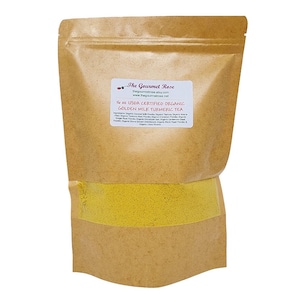 Puede incluir: Una bolsa de papel marrón de té de cúrcuma Golden Milk. La bolsa tiene una etiqueta blanca con el texto "The Gourmet Rose" y "16 oz USDA Certified Organic Golden Milk Turmeric Tea". El té es un polvo amarillo brillante.