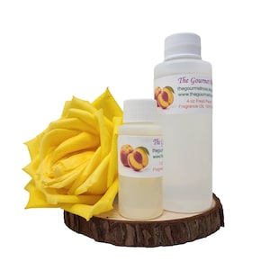 Peut inclure: Deux flacons blancs d'huile parfumée avec des illustrations de pêches et du texte, à côté d'une grande rose jaune sur une tranche de bois. Les flacons sont étiquetés "The Gourmet" et "Fresh Peach Fragrance Oil."