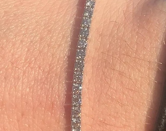 May include: A silver tennis bracelet with small, clear stones.