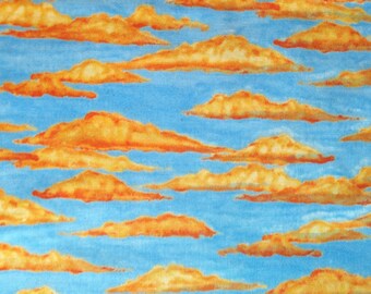 Puede incluir: Una tela con un patrón repetitivo de nubes naranjas y amarillas sobre un cielo azul claro. Las nubes tienen una apariencia texturizada, con variaciones de color y forma, creando un diseño caprichoso y artístico.