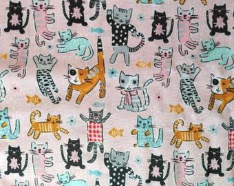 Puede incluir: Tela rosa con un patrón repetido de gatos de dibujos animados en varias poses y colores, incluyendo negro, naranja, gris y azul. Los gatos están intercalados con pequeños peces y flores. La tela tiene un diseño juguetón y caprichoso.