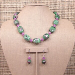 May include: A green and pink gemstone necklace and earrings set. The necklace is made of oval-shaped green gemstones with pink accents. The earrings are dangle earrings with a single green gemstone with pink accents.