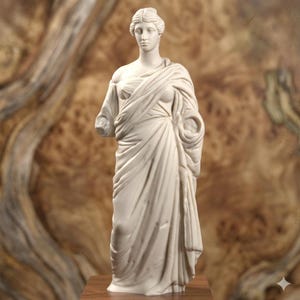 May include: A white marble statue of a draped female figure, missing one arm. The statue has detailed facial features and is standing on a wooden surface. The background is a warm, wood-grain pattern.