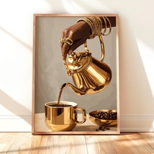 May include: A framed art print shows a golden teapot pouring coffee into a matching mug. The image features a hand with gold jewellery, holding the teapot. A small bowl of coffee beans is also visible. The artwork has a warm, luxurious aesthetic.
