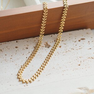 May include: A gold-toned chain necklace featuring a repeating leaf or vine-like link pattern. The metal links are textured and arranged in a continuous, symmetrical design that creates a delicate, organic appearance throughout the entire length.