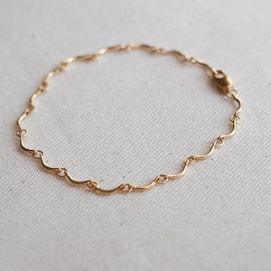 May include: A delicate gold chain bracelet featuring a series of interconnected, wavy, S-shaped links. The bracelet is circular in shape and includes a small, secure lobster claw clasp mechanism for fastening, showcasing a polished metallic finish.