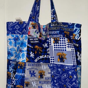 May include: A blue and white patchwork tote bag with the Kentucky Wildcats logo and various slogans, including "Go Big Blue", "See Blue", and "Kentucky Wildcats".