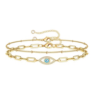 Puede incluir: Un conjunto de dos pulseras de cadena dorada con un dije de ojo azul malvado. El dije está rodeado de diamantes de imitación transparentes.