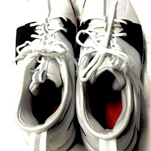 May include: A pair of white athletic shoes with black accents and white laces. The shoes have a mesh-like texture on the upper and a red interior. The soles are white with a gray stripe.