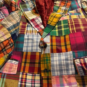 Peut inclure: Un blazer patchwork avec divers motifs à carreaux aux couleurs vives, notamment le rouge, le vert, le jaune et le bleu. Le blazer a un design classique avec un revers cranté, deux poches avant et une fermeture à bouton. La doublure intérieure est de couleur bordeaux unie.