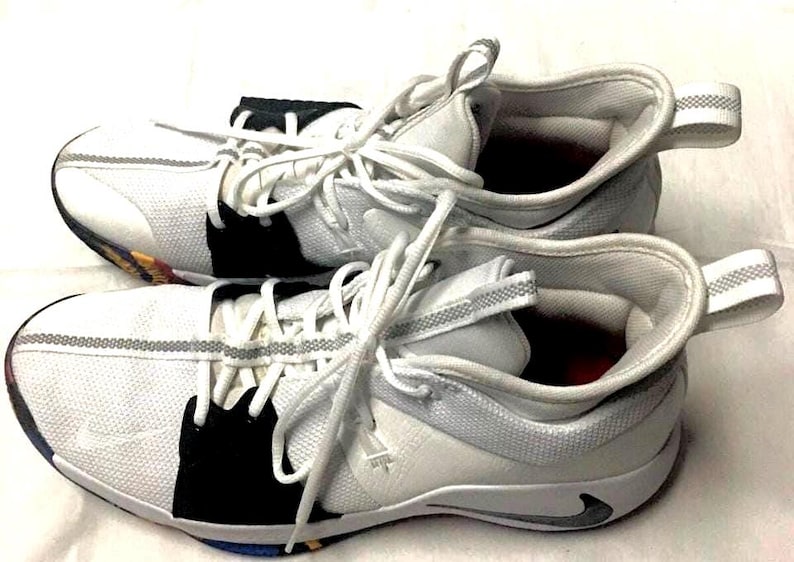 May include: Pair of white and gray athletic shoes with white laces. The shoes have black accents and a gray stripe detail. The soles have a multi-colored design. The shoes are designed for athletic activities.