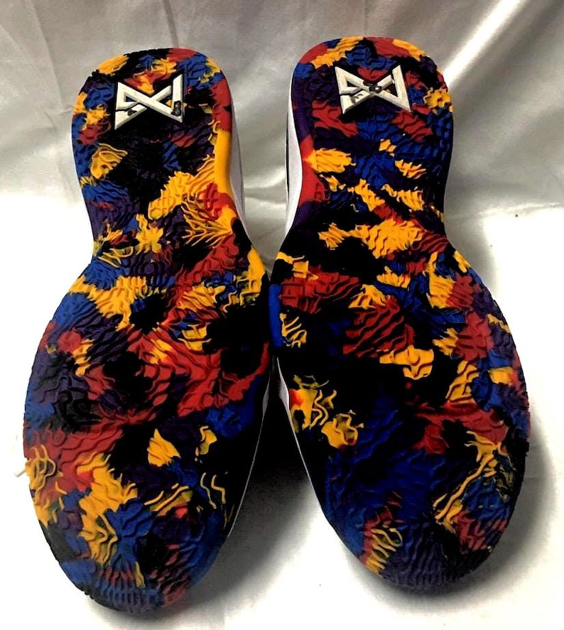 May include: Pair of athletic shoes with colorful soles. The soles feature a vibrant pattern of red, yellow, blue, and black shapes. The white midsoles have a red accent. The heel area displays a white logo.
