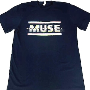 Puede incluir: Una camiseta negra con la palabra "MUSE" en letras blancas con un efecto glitch. El texto "SIMULATION THEORY" está impreso en letras blancas más pequeñas debajo de la palabra "MUSE".