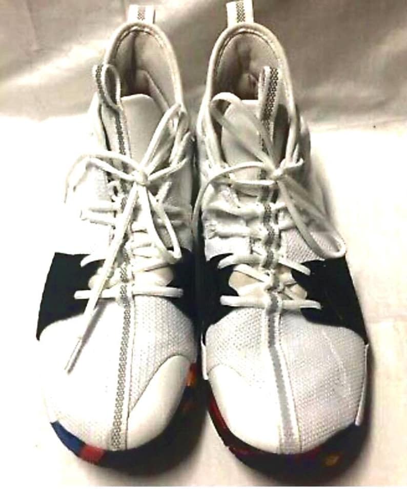 May include: Pair of white athletic shoes with black accents and white laces. The shoes have a mesh-like texture on the front and sides, with a colorful sole. The design includes a padded tongue and collar for comfort.