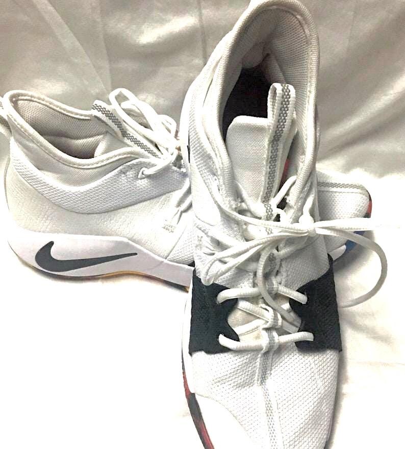 May include: White athletic shoes with black accents and a black Nike swoosh. The shoes have white laces and a black strap across the top of the foot. The soles are white with a black and red accent.