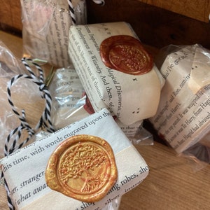 May include: A close-up of three wrapped gifts with a gold and red wax seal featuring a tree design. The gifts are wrapped in white paper with black and white string. The text on the gifts reads "Developments in Wizardry. And then, of the most important Magical Discoveries, and from Important Magical Discoveries, and", "Now they were facing this time, with words engraved upon the", and "There were shops and strange silver robes, showing instructions that were",  "There were shops and strange silver robes, showing instructions that were".