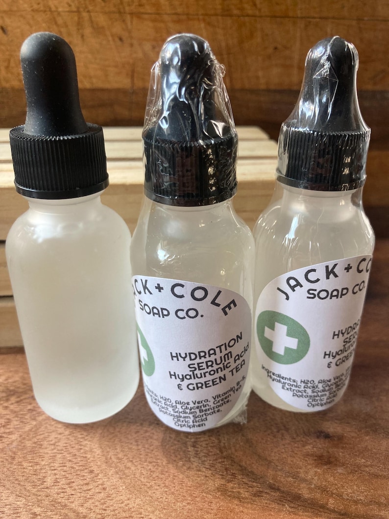 May include: Three clear glass bottles with black dropper tops and white labels. The labels have green accents and text that reads "Jack + Cole Soap Co." and "Hydration Serum Hyaluronic Acid & Green Tea".