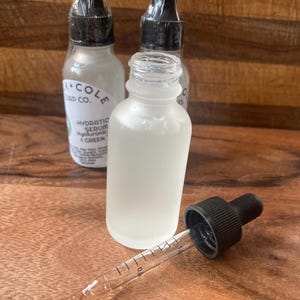 May include: Three glass bottles with dropper tops filled with a clear liquid. The bottles are labeled "Oak + Cole Soap Co." and "Hydrating Serum Hyaluronic Acid + Green Tea".