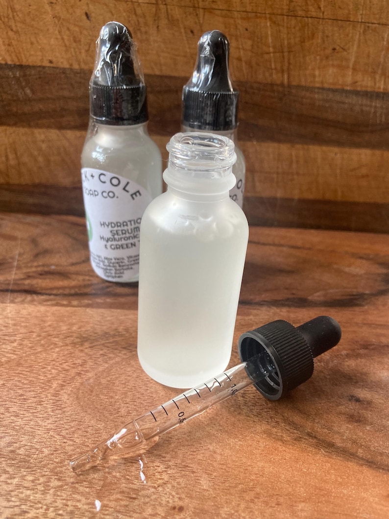 May include: Three glass bottles with dropper tops filled with a clear liquid. The bottles are labeled "Oak + Cole Soap Co." and "Hydrating Serum Hyaluronic Acid + Green Tea".