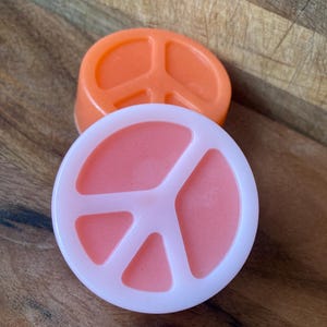 May include: Two peace sign shaped soap bars. One is orange and the other is pink.